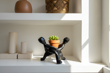 Decorative black sculpture of two people holding a pot with a plant on a shelf.