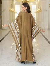 Woman wearing a long beige patterned kaftan dress in a reflective indoor setting