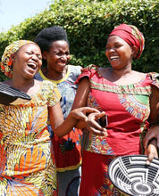 Three women in colorful traditional african attire laughing outdoors.