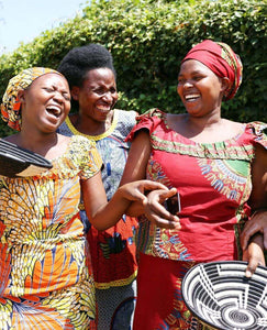 Three women in colorful traditional african attire laughing outdoors.