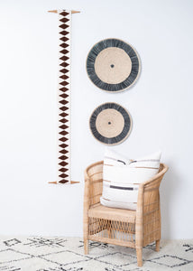 Wicker chair with a striped pillow, decorative circular wall art, and a growth chart on a white wall.