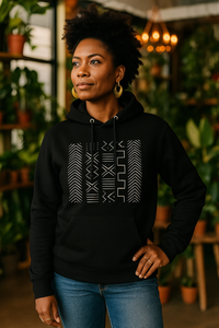 Person wearing a black hoodie with a geometric pattern in a plant-filled room