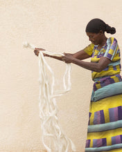 Woman in colorful traditional african attire holding sisal strands against a beige wall
