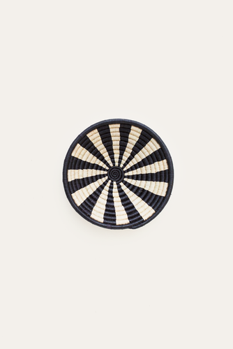 Round woven basket with black and white striped pattern on a beige background
