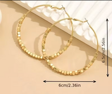 Gold hoop earrings with bead detailing on a beige surface, shown with measurements.