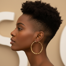 Gold hoop earrings with bead detailing on a beige surface