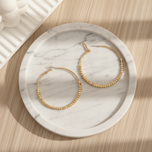 Gold hoop earrings on a marble tray with a wooden surface