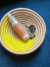 Coiled beige and bright yellow handmade basket with a bottle and keys in it