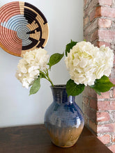 Blue ceramic vase with white flowers against a brick wall and decorative basket background