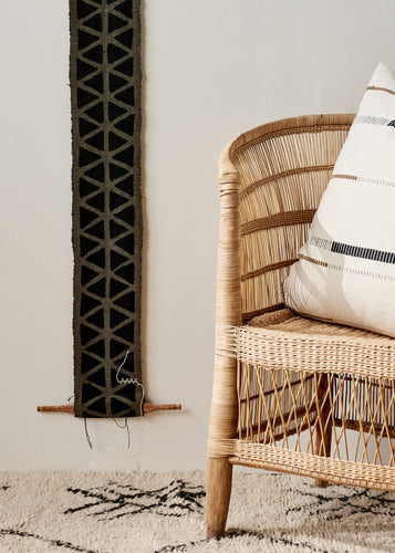 african fabric wall art hung up. Wicker chair with a pillow in the room.