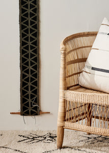 african fabric wall art hung up. Wicker chair with a pillow in the room.
