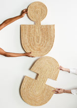 Two woven wall art pieces shaped like 'U' and 'S' held by hands on a white background