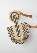 Person holding a round woven mat art with black and beige pattern on a white background