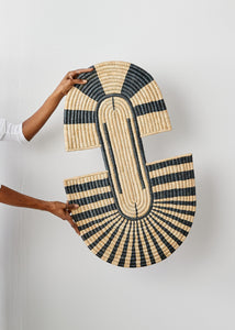 Woven wall art piece with black and beige pattern held by a person against a white background