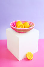 Pink woven basket with lemons on a white block against a purple background