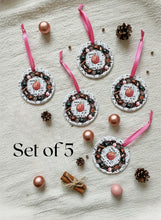 Set of 5 decorative pink ornaments with ribbons on a textured surface with small pinecones and pink balls.