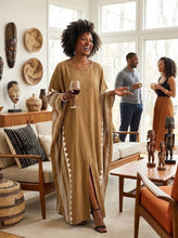 Woman in a beige dress holding a glass of wine in a living room with a man and another woman in the background.