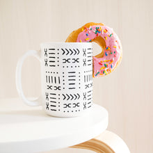 White coffee mug with black African design next to a donut