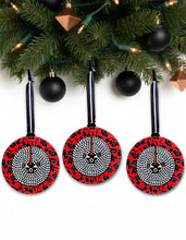 Three circular red and black patterned ornaments hanging on a Christmas tree.