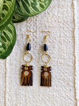 Wooden hand-shaped earrings with black beads on a textured fabric background