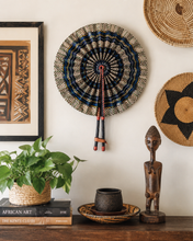 Decorative wall art with woven circular designs, books, a plant, and a wooden figurine on a shelf.