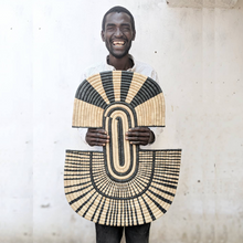 Man holding a large woven basket with geometric pattern against a light background