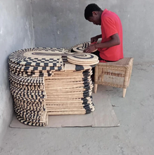 Person working with woven materials on a concrete floor against a gray wall.
