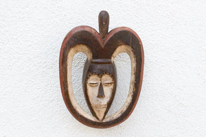 Decorative wall hanging with a heart-shaped design and face on a textured white background