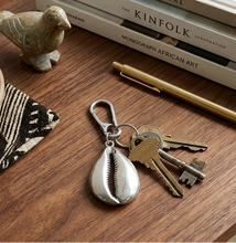 Keychain with keys on a wooden surface next to books and a pen