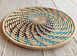 Woven trivet with black and blue pattern on a textured surface