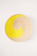 Round woven basket with yellow and beige spiral pattern on a white background
