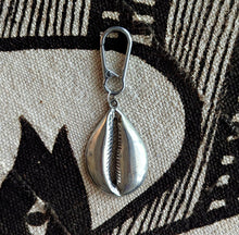 Silver cowrie shell key chain bag charm pendant with a clasp on a textured fabric background