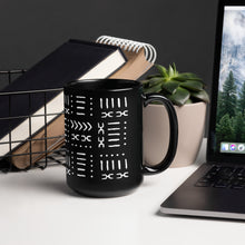 Black mug with a black and white African pattern on a desk with a laptop and books.