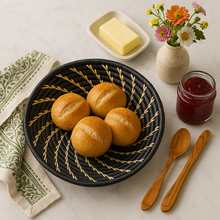 Woven basket with bread rolls on a table with butter, jam, and flowers.
