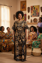 Woman in a black and gold patterned kaftan dress standing in a room with other women at a kaftan party