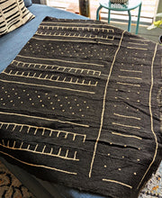 Black mud cloth fabric with abstract patterns draped over a blue couch.