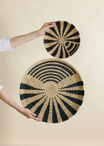 Two woven baskets with black and beige patterns held by a person against a beige background