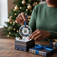 Person holding a decorative ornament with a Christmas tree in the background