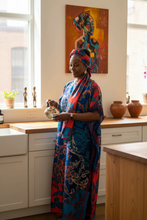Woman in a colorful dress standing in a kitchen with a painting on the wall.