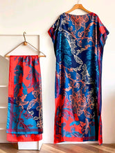 Blue floral-patterned kaftan dress with scarf on hangers against a white wall.