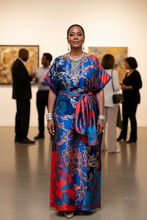 Woman in a colorful kaftan dress standing in an art gallery with other visitors.