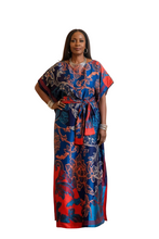 Woman in a blue and red patterned dress standing in an indoor setting with people in the background.