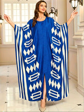 Woman wearing a blue kaftan dress with white geometric patterns in an indoor setting.