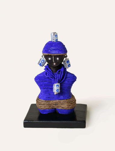 Handmade figurine of a person wearing a blue beaded outfit with decorative elements on a white background
