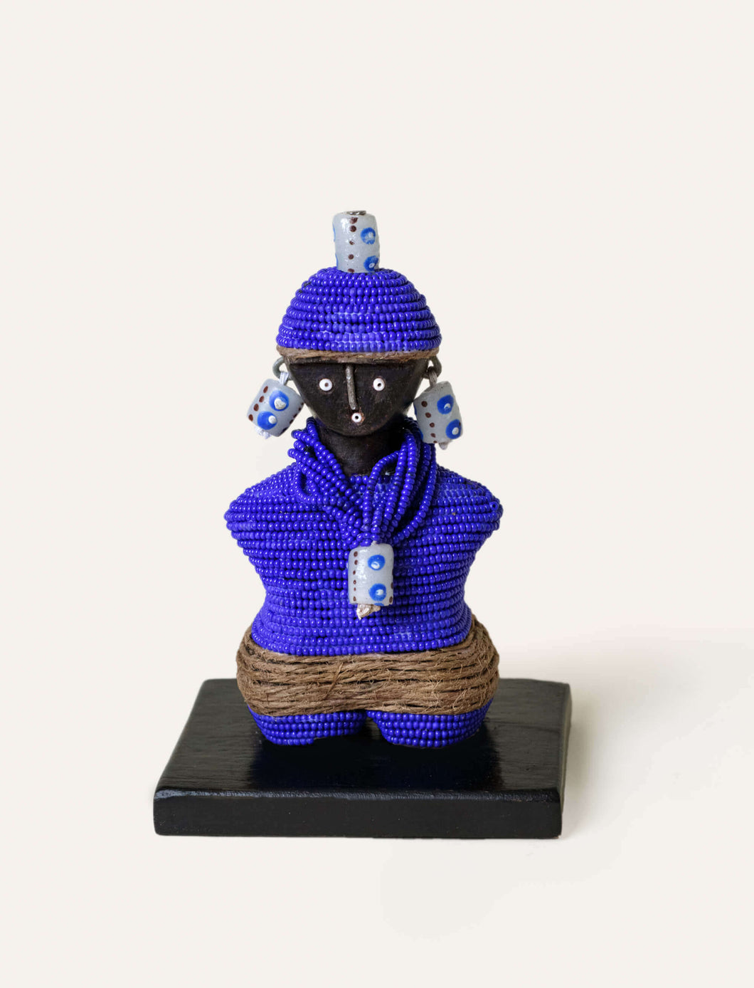 Handmade figurine of a person wearing a blue beaded outfit with decorative elements on a white background