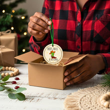 Person holding a cowgirl Christmas ornament with a tree and presents in the background