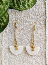 Gold earrings with white half-circle stones on a textured fabric background