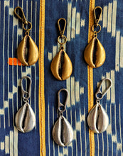 Gold and silver shell-shaped keychains on a blue and yellow striped background