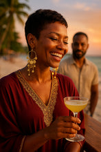 Woman wearing statement dangle earrings holding a cocktail on a beach with a man in the background