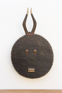 Decorative wall mask with antlers and a circular base on a white background